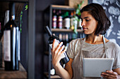 Wine store female worker reading wine bottle label