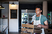 Thoughtful young Latin American grocery store worker holding wooden crate