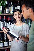 Weinhändlerin hält eine Weinflasche in der Hand, während sie mit einem Kollegen spricht