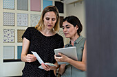 Medium shot of two female home decoration business owners choosing colors from color swatches
