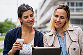 Mittelaufnahme von zwei Unternehmerinnen, die ihre Arbeit auf einem digitalen Tablet überprüfen, während sie im Freien arbeiten