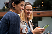 Mid-shot side view of two female entrepreneurs checking messages from their followers on their smartphones