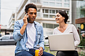 Mid-shot of diverse couple of co-workers discussing business matters while working outdoors