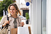 Mittlere Einstellung einer lächelnden jungen Frau, die Einkaufstüten auf der Straße trägt