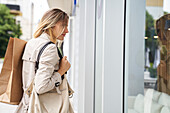 Side view shot of woman carrying bags while window shopping