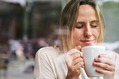 Porträt einer Frau mit geschlossenen Augen, die eine Tasse Kaffee genießt