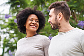 Mid-shot portrait of an African-American woman and Caucasian man smiling at each other and having a good time outdoors