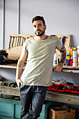 Young adult male mechanic leaning on workbench