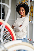 Porträt einer afroamerikanischen Fahrradladenbesitzerin, die in ihrem Laden steht und in die Kamera lächelt (mittlere Aufnahme)