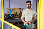 Porträt eines bärtigen Mannes, der in seiner Werkstatt vor seinen Werkzeugen steht (halbnah)