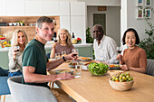 Group of diverse senior friends gathered together for lunch in the kitchen