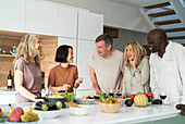 Diverse group of senior friends gathered at kitchen counter while drinking wine