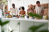 Verschiedene Gruppen von Freunden, die sich in der Küche amüsieren, während sie sich zum Essen fertig machen