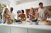 Diverse Freunde mittleren Alters, die sich in der Küche unterhalten, während sie das Abendessen zubereiten