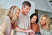 Diverse group of senior friends using smart phone at kitchen