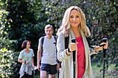 Blonde ältere Dame mit Rucksack und Wanderstöcken beim Wandern im Wald mit einer Gruppe von Freunden