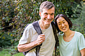 Middle-aged diverse couple looking at camera while hiking out in the woods