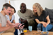 Lustige Gruppe von Freunden mittleren Alters, die sich zu Hause Fotos auf dem Mobiltelefon ansehen