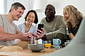 Mann mittleren Alters zeigt seiner Gruppe verschiedener Freunde zu Hause ein Foto auf seinem Handy
