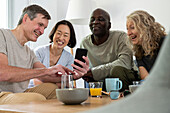 Middle-aged man showing a photo on his phone to his group of diverse friends indoors