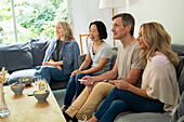 Verschiedene Gruppen von Freunden sitzen auf der Couch und sehen fern