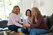 Portrait of three senior ladies having a good time together watching photos on mobile phone at home