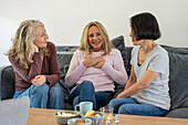 Drei ältere Freundinnen unterhalten sich zu Hause auf dem Sofa sitzend
