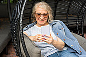 Portrait of senior lady sitting in lounge chair looking at cell phone