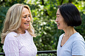 Side view shot of senior Asian-American woman and her friend smiling at each other while standing outdoors