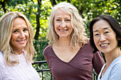 Porträt von drei Freundinnen mittleren Alters, die in die Kamera schauen, während sie sich im Freien amüsieren