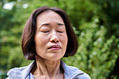 Asiatische Seniorin mit geschlossenen Augen in einem Haus stehend
