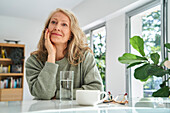 Smiling senior woman looking up while sitting with hand on chin