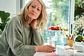 Thoughtful senior woman with hand behind neck sitting in dining room