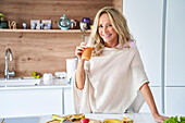Blonde Frau mittleren Alters genießt Fruchtsaft zu Hause