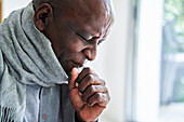 Älterer afroamerikanischer Mann, der einen Schal trägt und in seine Hand hustet