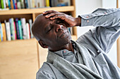 Afroamerikanischer Mann mittleren Alters hält sich vor Schmerzen den Kopf