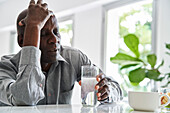 Afroamerikanischer Mann mittleren Alters mit Kopfschmerzen bei der Einnahme seiner Medikamente