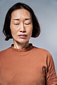 Reife asiatische Frau mit geschlossenen Augen vor weißem Hintergrund
