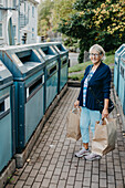 Frau mit Papiersäcken an Recyclingtonne