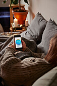 Frau im Bett liegend und Temperatur-App nutzend