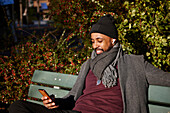 Mann sitzt auf einer Bank und telefoniert im Herbstpark