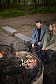 Couple preparing hotdogs over campfire