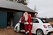 Mann im Weihnachtsmannkostüm steht neben einem Auto