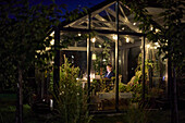 Woman sitting in illuminated greenhouse