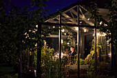 Woman sitting in illuminated greenhouse