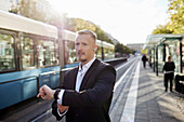 Businessman waiting at tram stop and checking watch