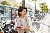 Smiling businesswoman using smart phone and earphones