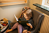 Mädchen sitzt zu Hause im Sessel und liest ein Buch