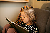 Mädchen sitzt im Sessel und liest zu Hause ein Buch