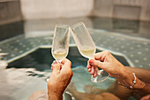 Hands holding champagne flutes in hot tub